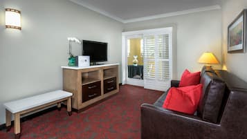 A living room with a flat-screen TV, a bench, a sofa with red cushions, and a lamp.