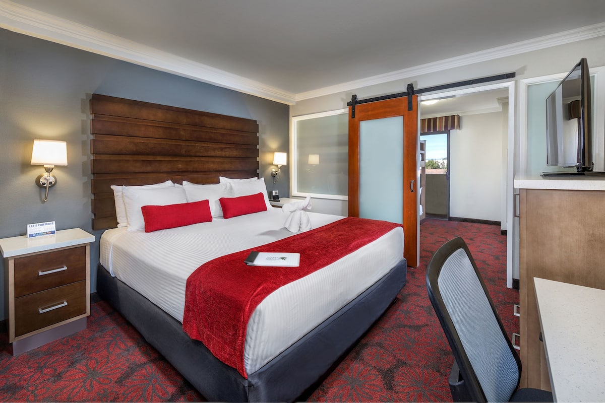 A hotel room with a large bed, a desk, and a mirror.