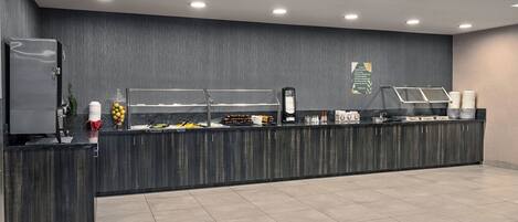 A modern breakfast bar with a dark wood finish, equipped with a refrigerator, a fruit bowl, and a coffee station.