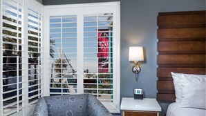 Une chambre d’hôtel avec un lit, une table de chevet avec une lampe, une chaise et une fenêtre avec des stores.