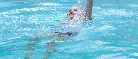 A person swimming in a pool with a stone wall and a metal ladder in the background.