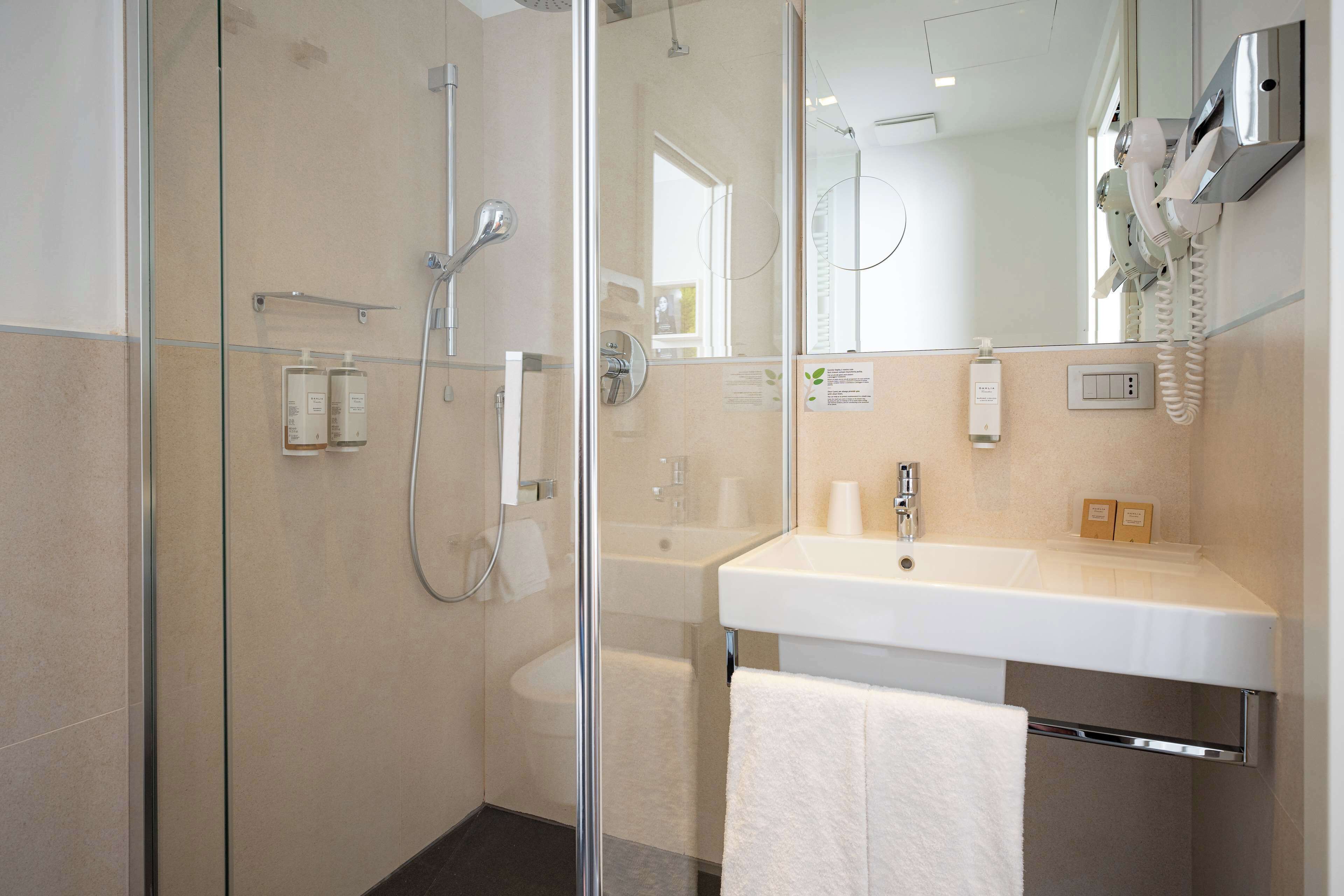 A modern bathroom with a glass shower enclosure, a white sink, and a mounted hairdryer.