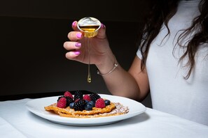 Une assiette de gaufres garnies de fruits rouges, avec du sirop versé dessus à partir d’un récipient en verre.