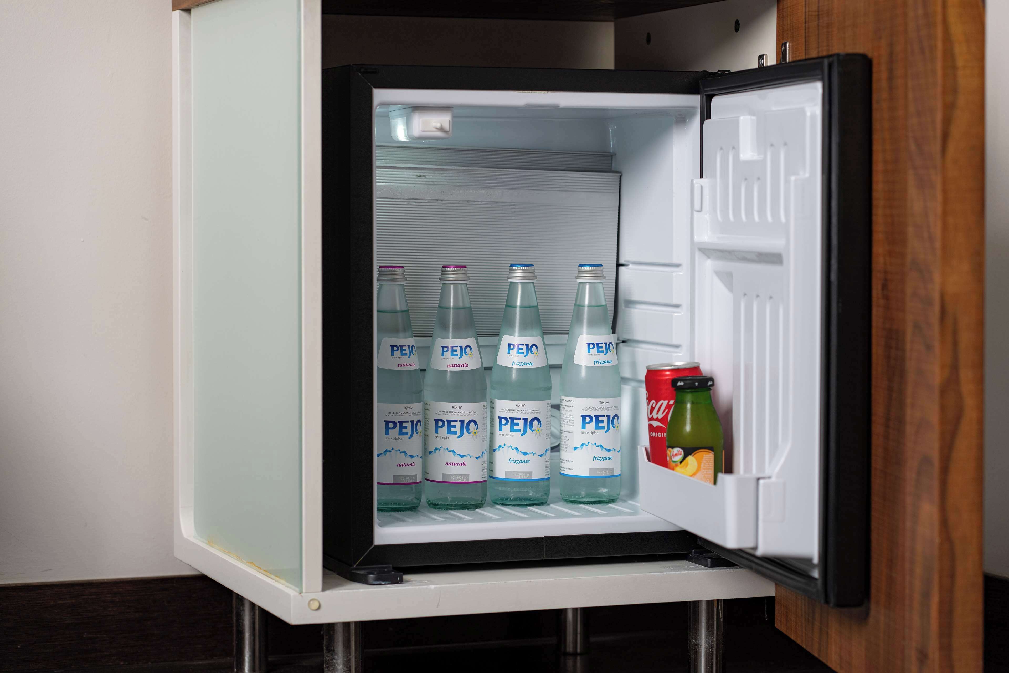 A mini-fridge with four bottles of PEJO water and a can of Coca-Cola.