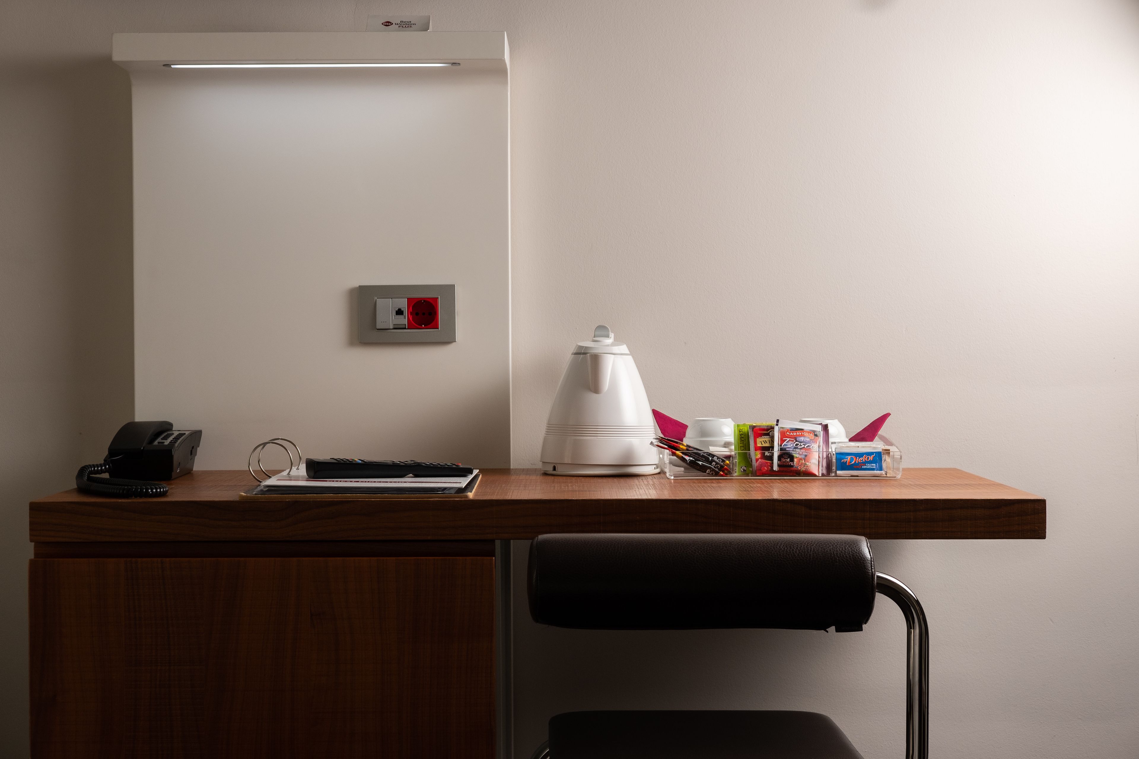 A desk with a telephone, a kettle, and some office supplies.