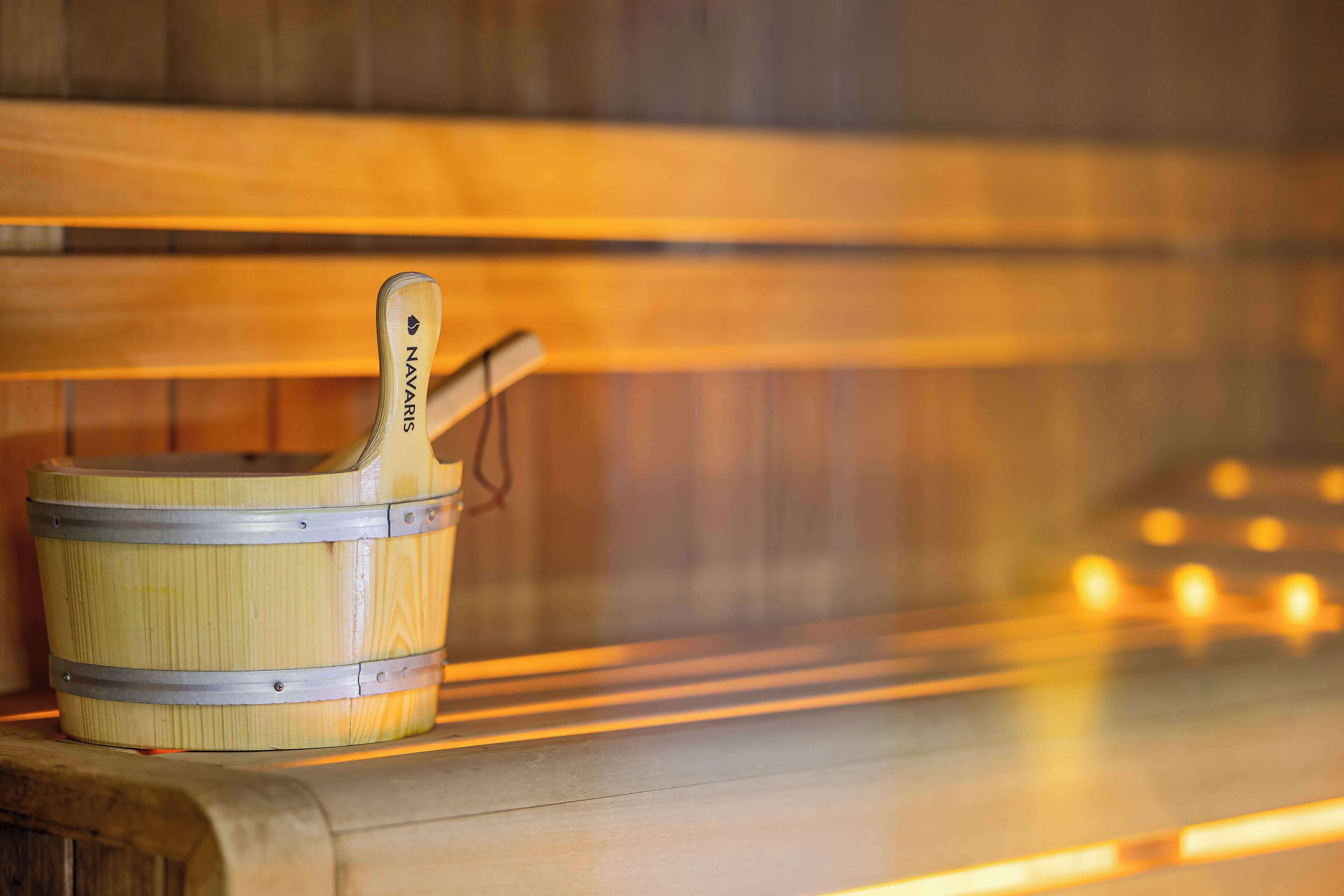 A wooden sauna with a wooden bucket and a metal handle, placed on a wooden bench.