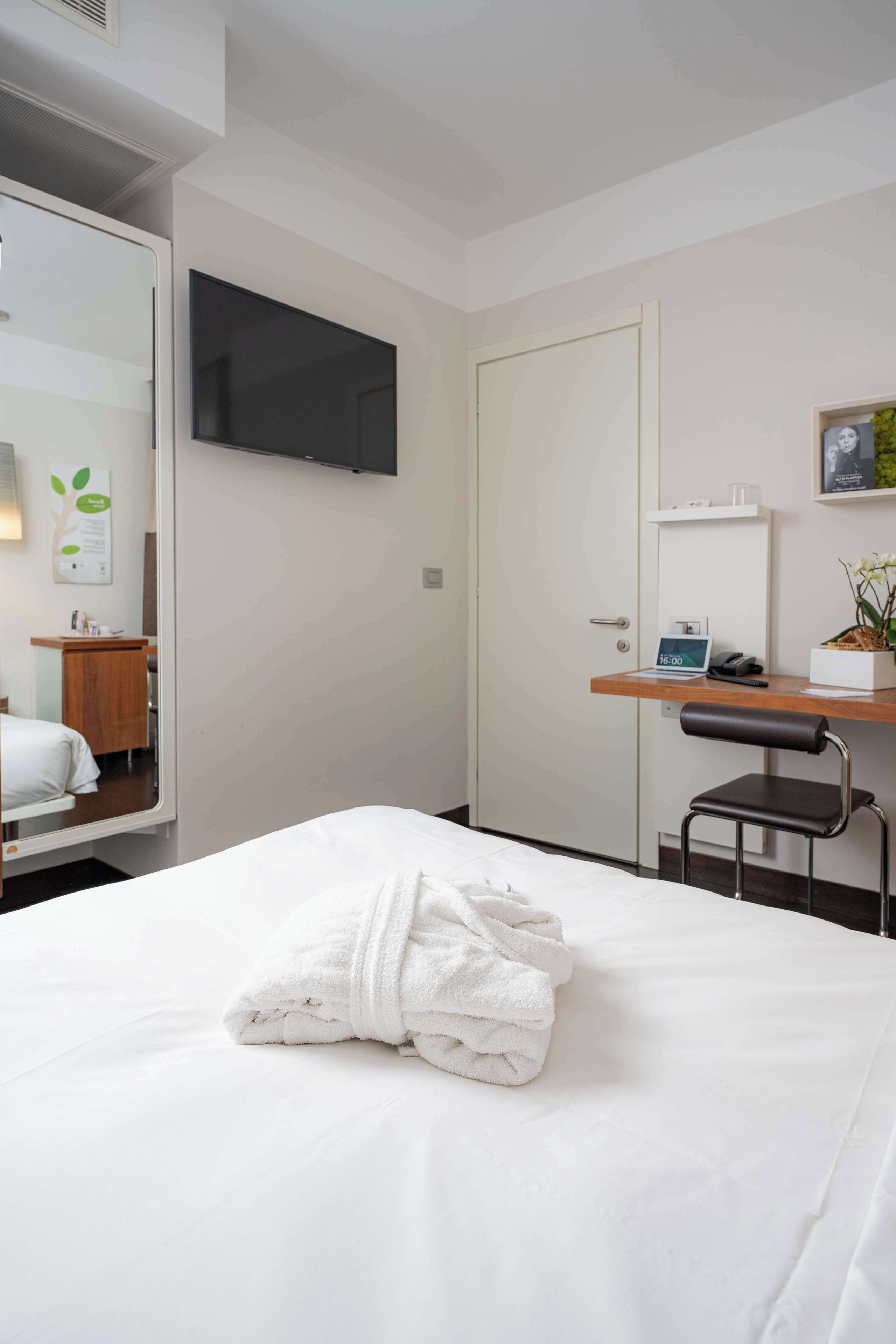 Una habitación de hotel con cama, escritorio, silla, televisor y puerta.