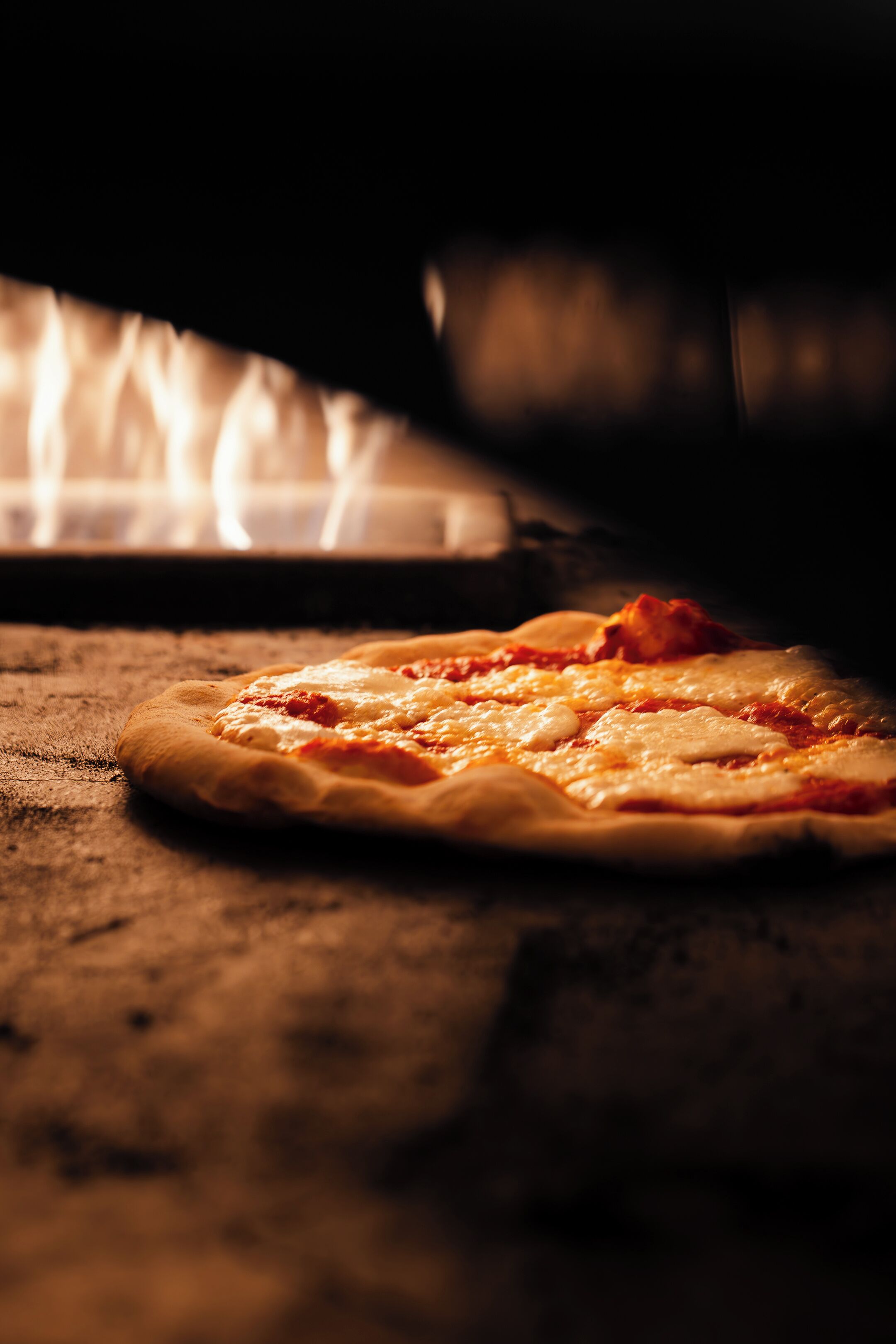 Pizza en horno de leña, con llamas visibles al fondo.