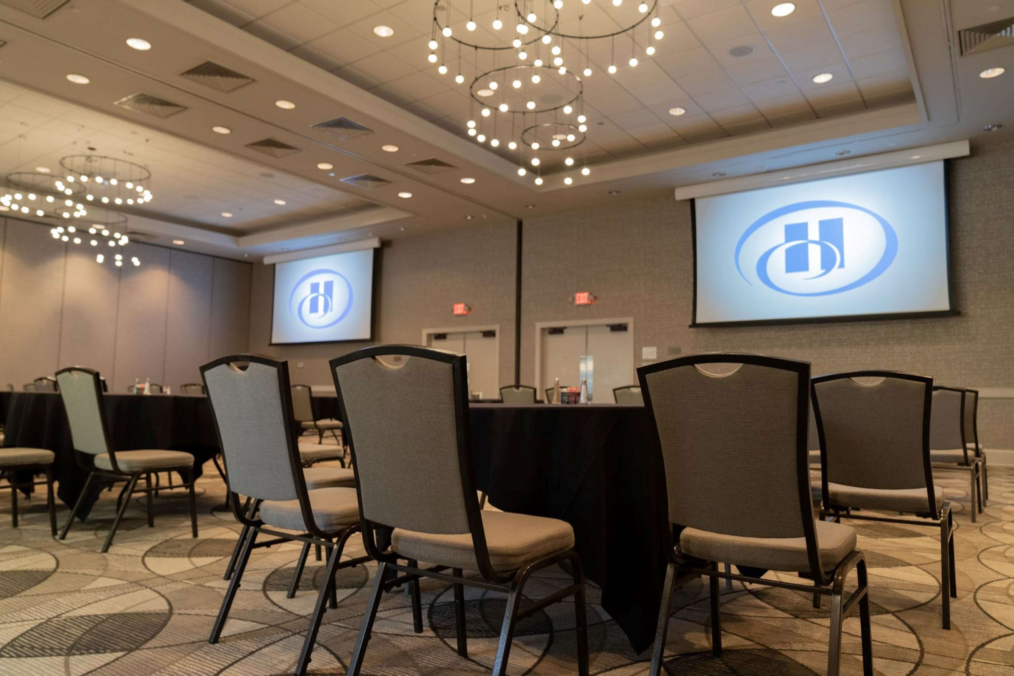 A conference room with a large screen displaying a logo, a table with chairs, and a chandelier.