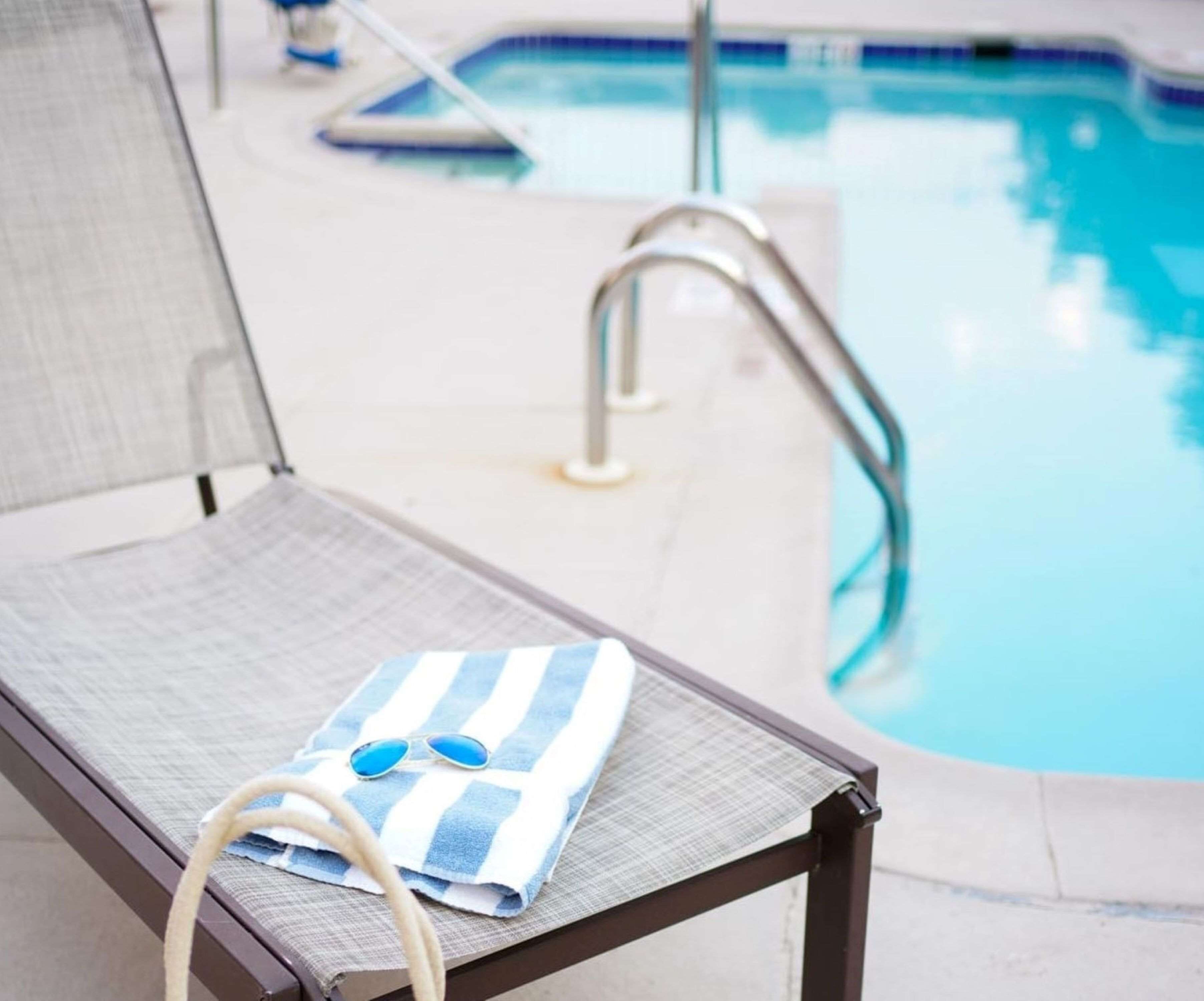 A poolside lounge chair with a towel and sunglasses, a pool, and a pool ladder.