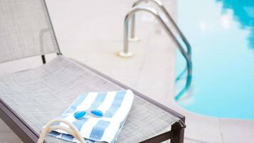 A poolside lounge chair with a towel and sunglasses, a pool, and a pool ladder.
