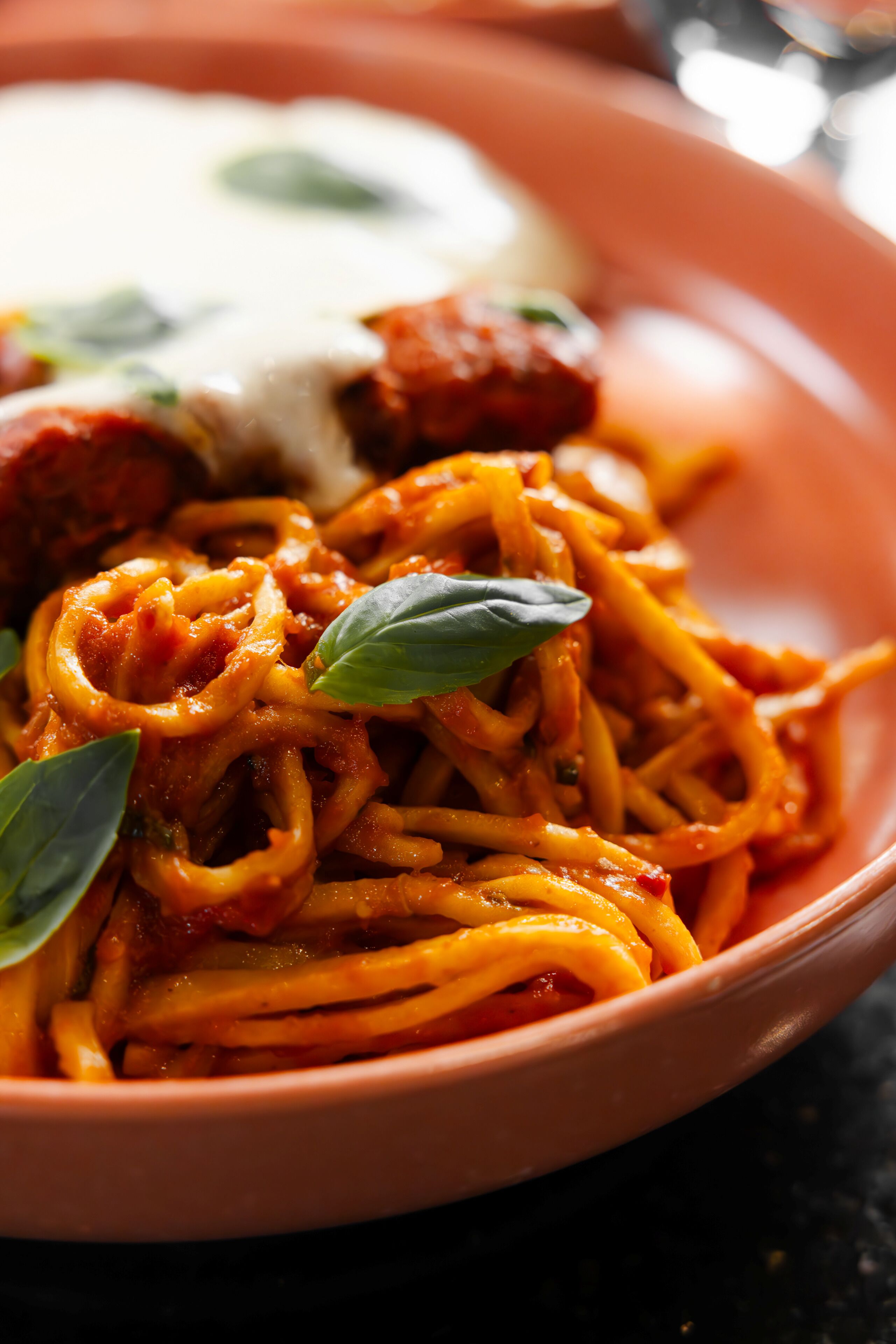 A bowl of spaghetti with a creamy sauce and basil leaves.