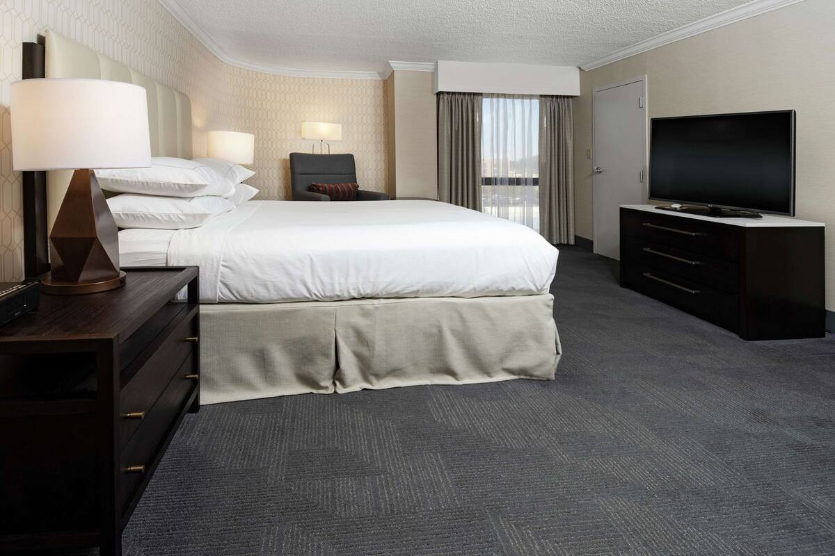 A hotel room with a bed, two bedside lamps, a TV, and a dresser.