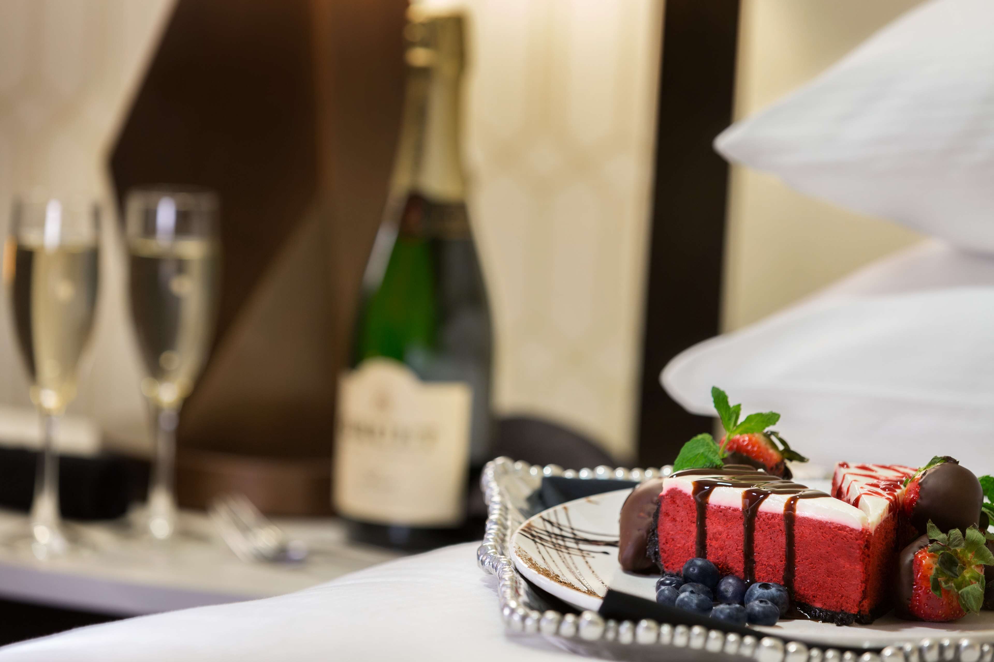 A dessert tray with a red cheesecake, strawberries, and blueberries, accompanied by champagne glasses and a bottle.