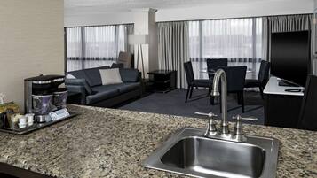 A hotel room with a granite countertop, a sink, a sofa, a dining table, and a flat-screen TV.