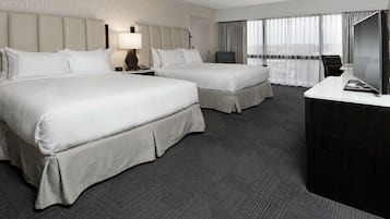 A hotel room with two beds, a desk, a TV, and a window with curtains.