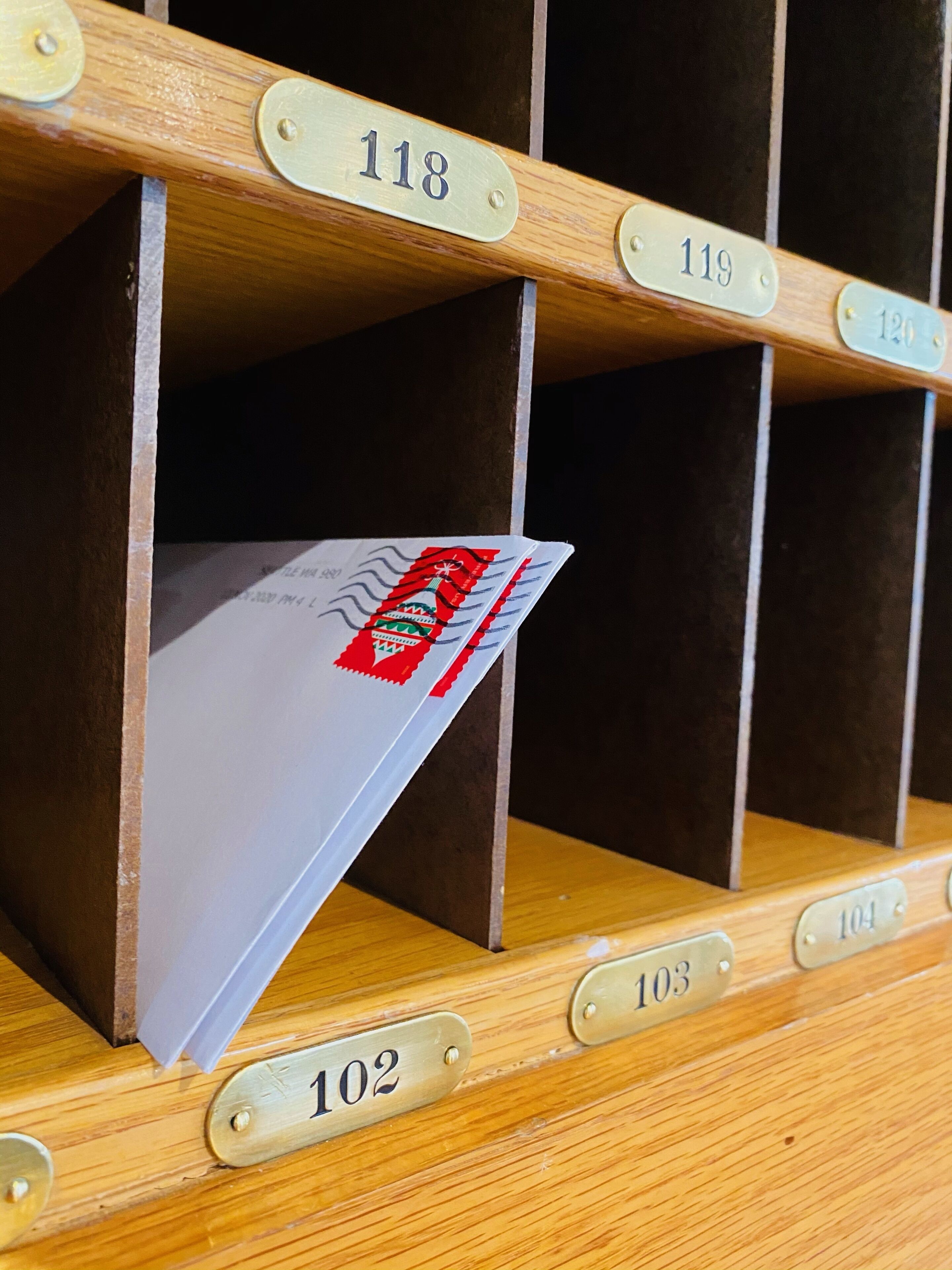 Una ranura de correo de madera con compartimentos numerados, uno de los cuales contiene una carta con un sello rojo.