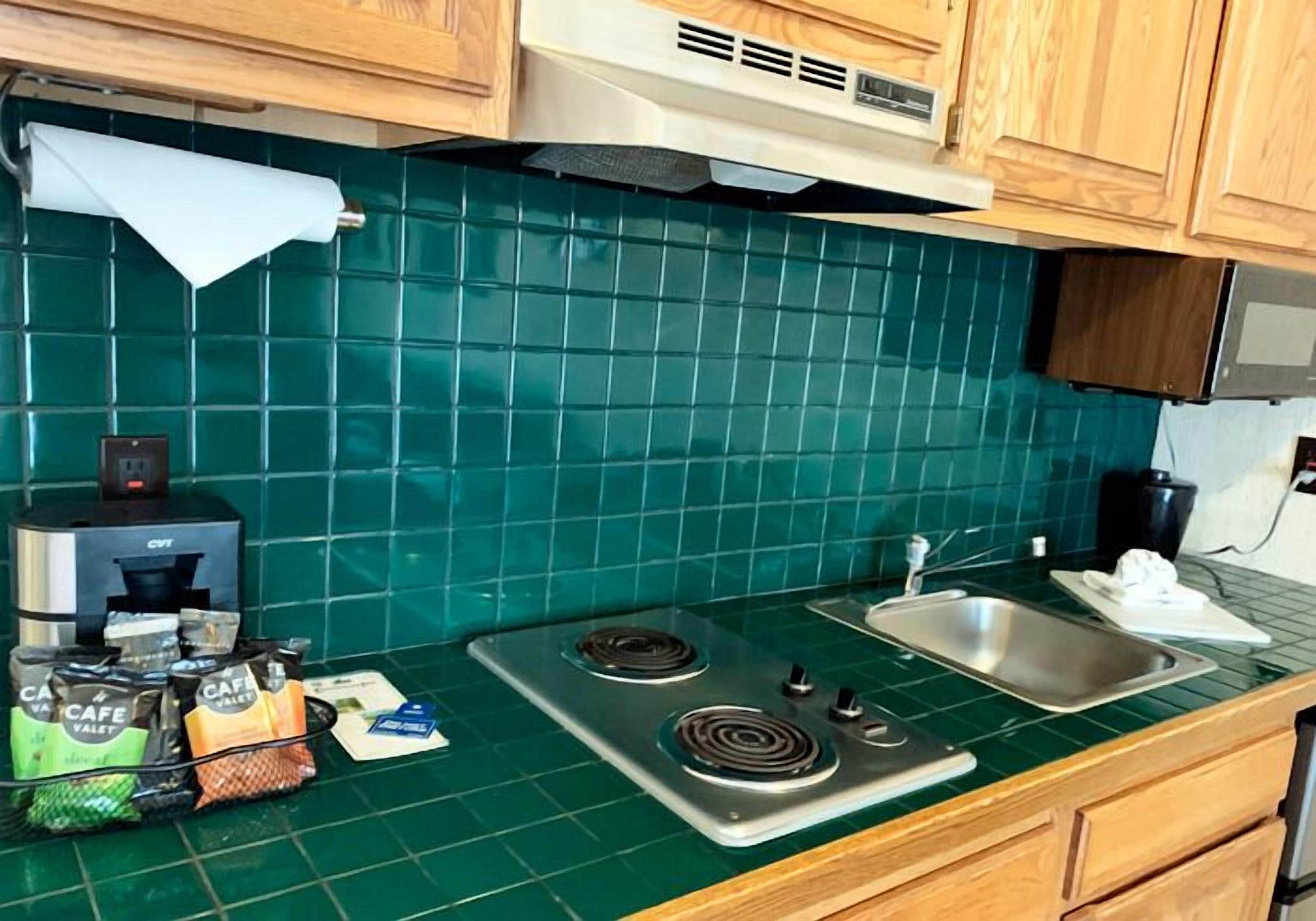 A kitchen with green tiles, a gas stove, a sink, and a coffee maker.