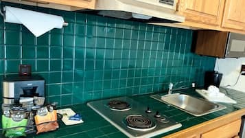 A kitchen with green tiles, a gas stove, a sink, and a coffee maker.