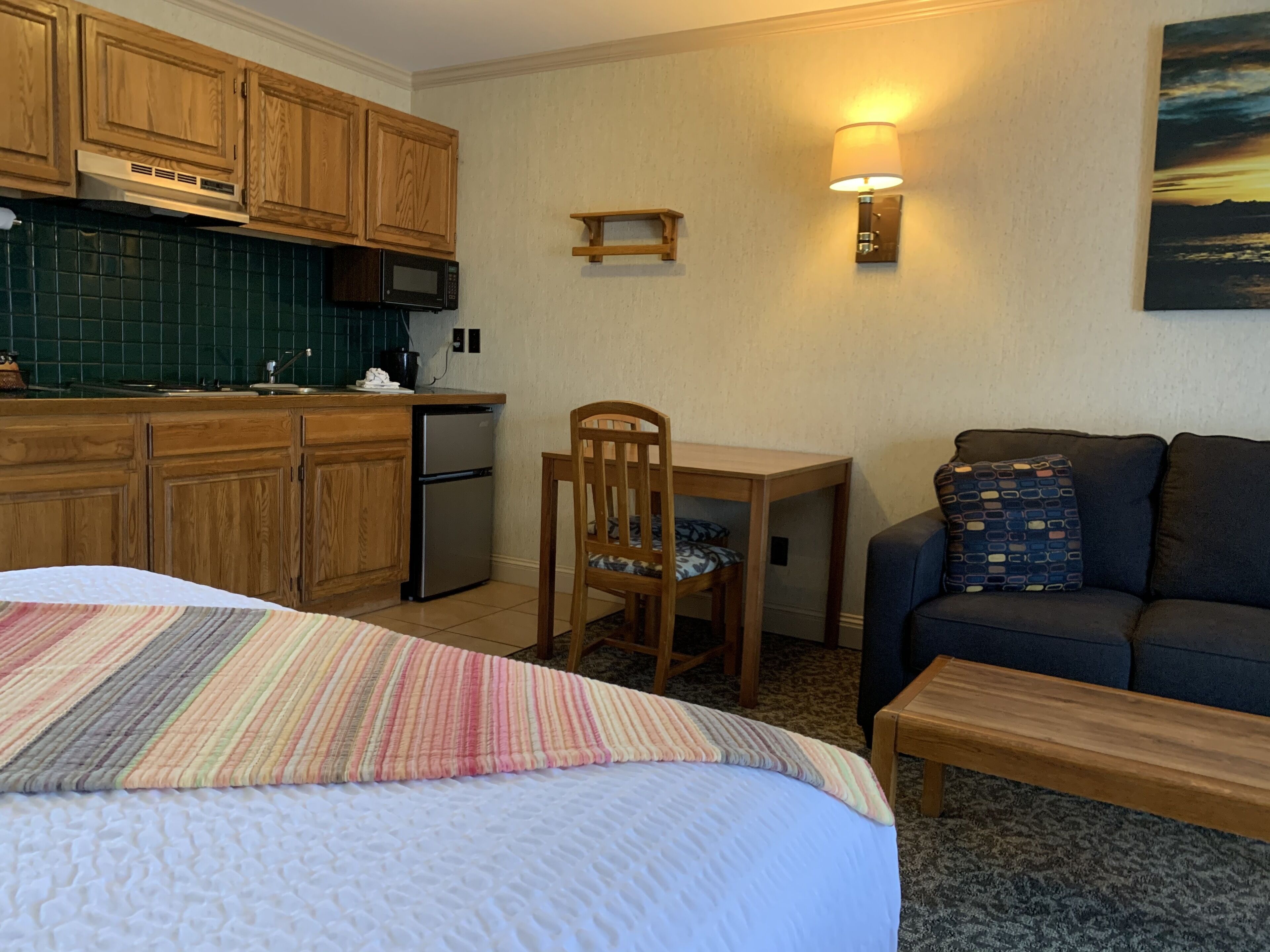 Ein Hotelzimmer mit einem Bett, einem kleinen Tisch, einer Couch, einer Küchenzeile und einem Bild an der Wand.