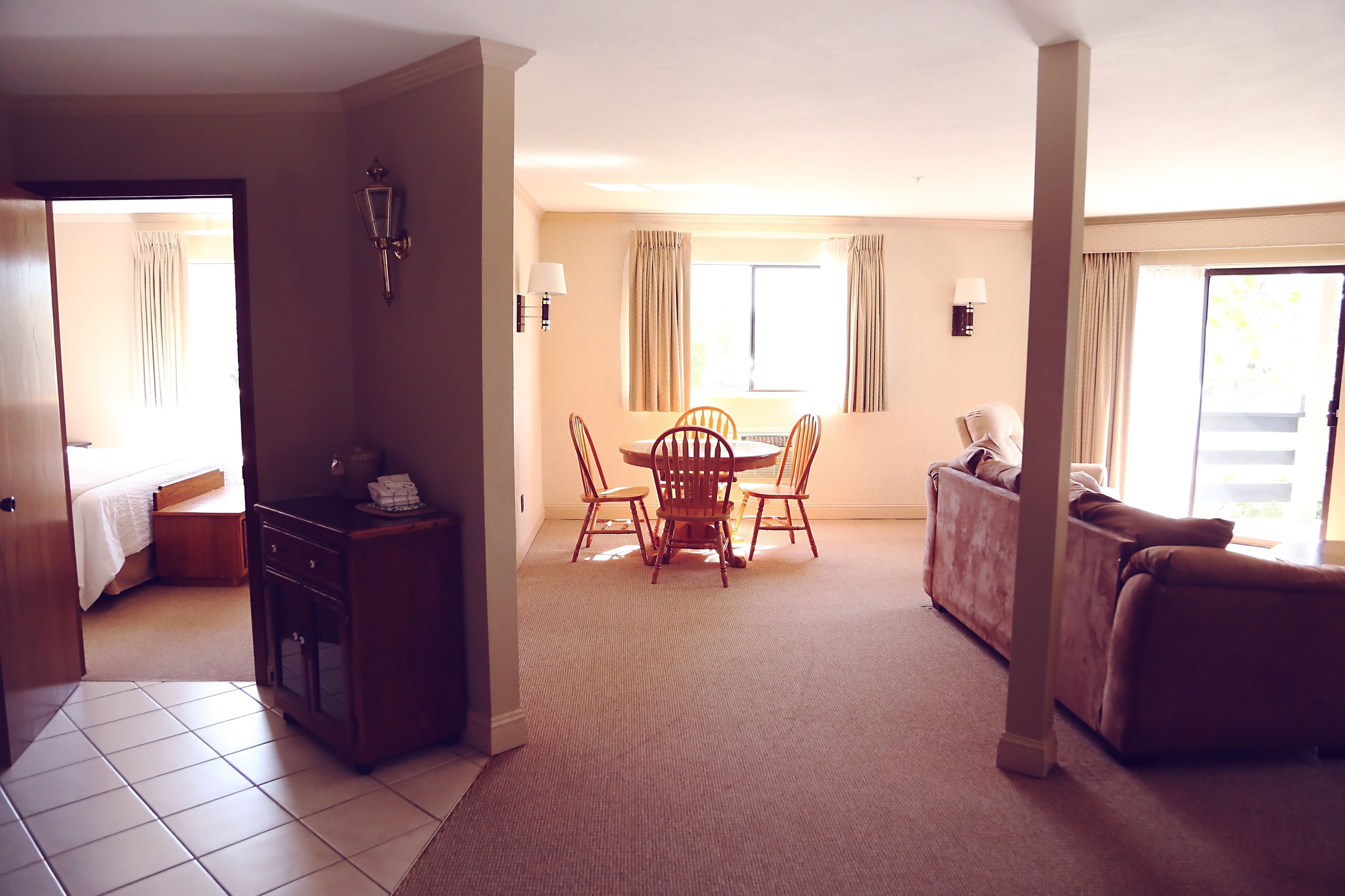 A hotel room with a dining area, a sofa, a cabinet, and a bed.