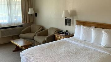 Una camera d'albergo con un letto grande, due poltrone, un tavolino, una lampada da comodino e una finestra con tende.