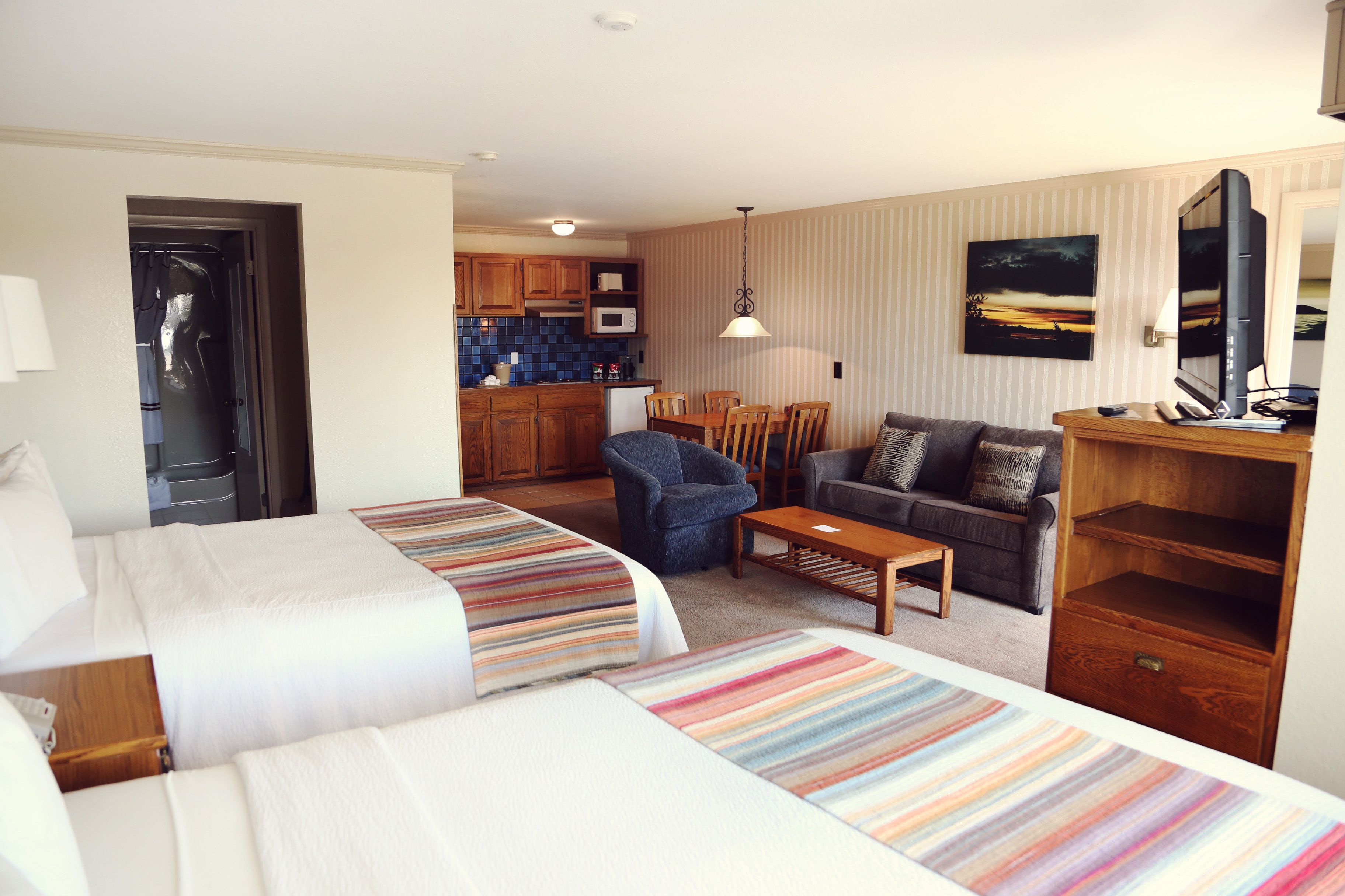Ett hotellrum med två sängar, en soffa, ett matbord och ett köksutrymme i bakgrunden.