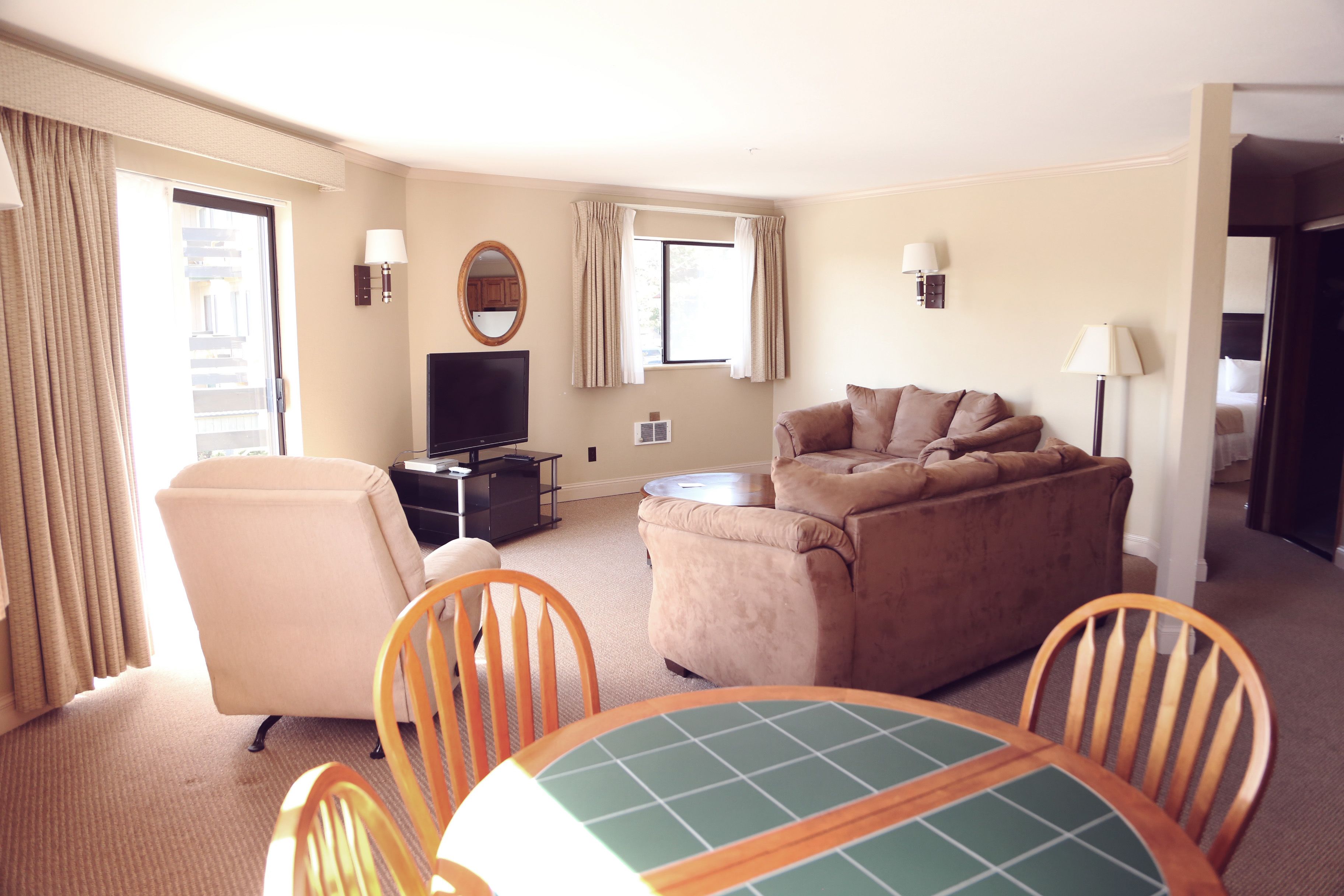 Une chambre d’hôtel équipée d’un canapé, d’une télévision, d’une table à manger avec des chaises et d’une fenêtre avec des rideaux.