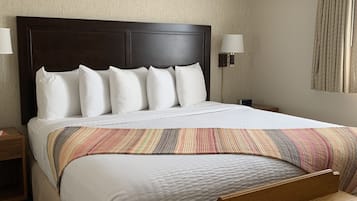 A hotel room with a large bed, two bedside lamps, a wooden nightstand, and a small wooden table.