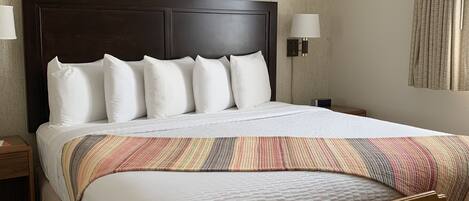 A hotel room with a large bed, two bedside lamps, a wooden nightstand, and a small wooden table.