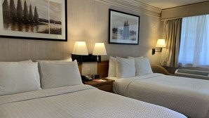 A hotel room with two beds, each with white bedding, two bedside lamps, and framed pictures on the wall. - Coachman Inn & Suites (Oak Harbor)