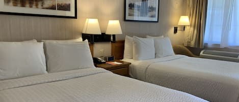A hotel room with two beds, each with white bedding, two bedside lamps, and framed pictures on the wall.