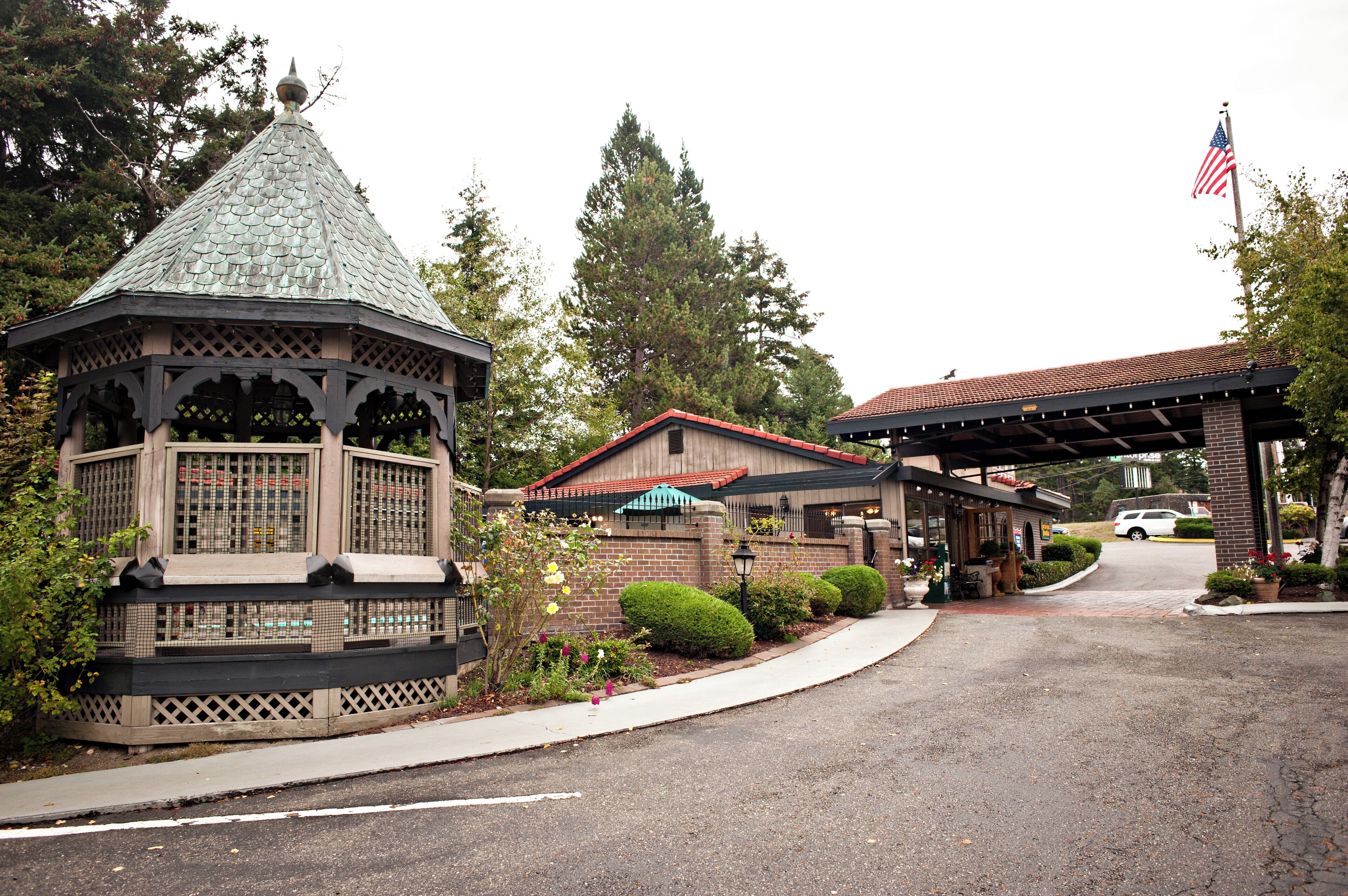 A gazebo with a tiled roof, a covered patio area, and a brick building with a red roof.