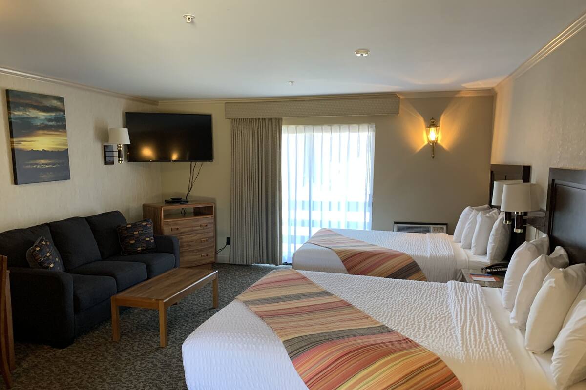 A hotel room with a sofa, two beds, a TV, a lamp, and a view of the outdoors.