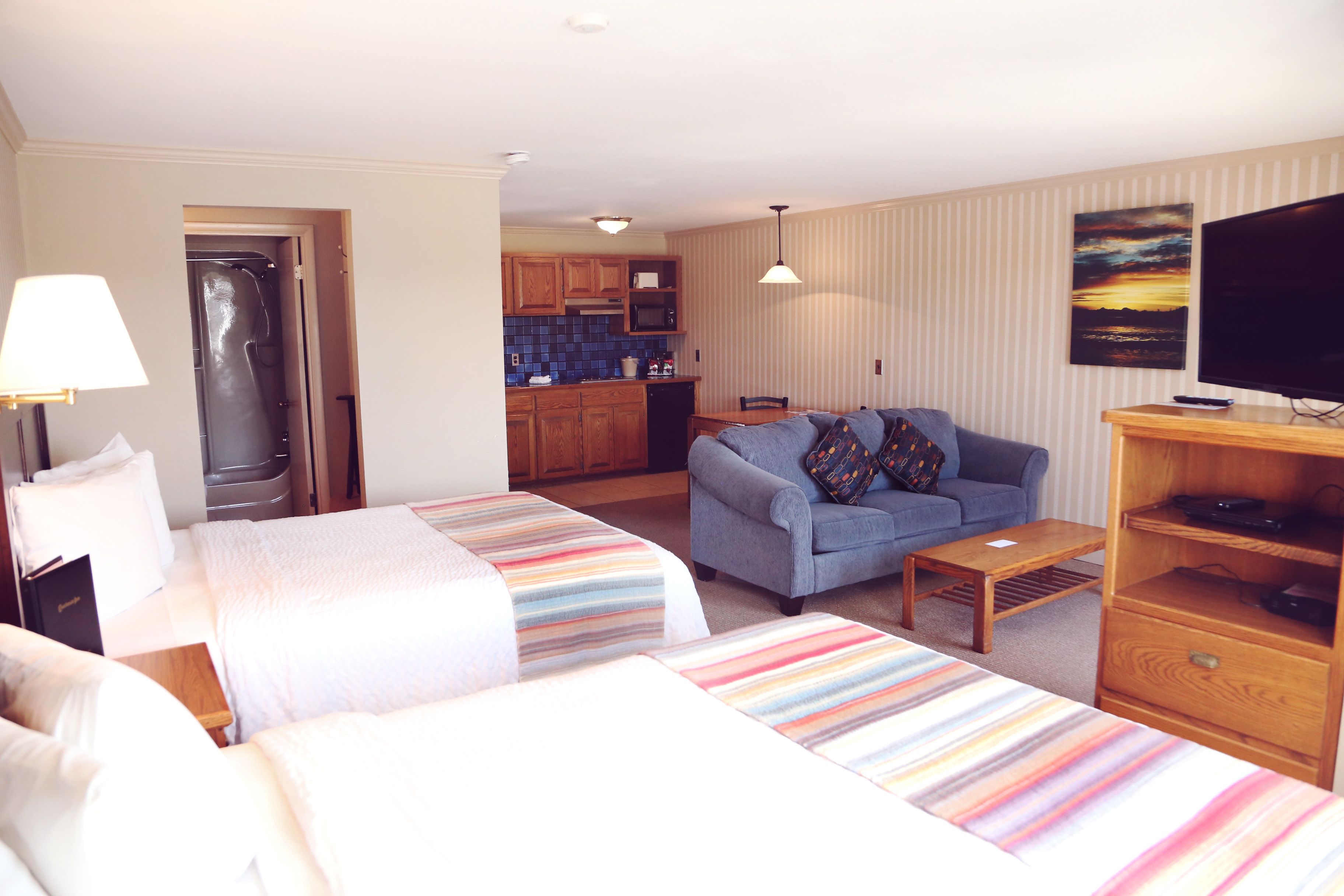 A hotel room with two beds, a sofa, a TV, and a kitchen area in the background.