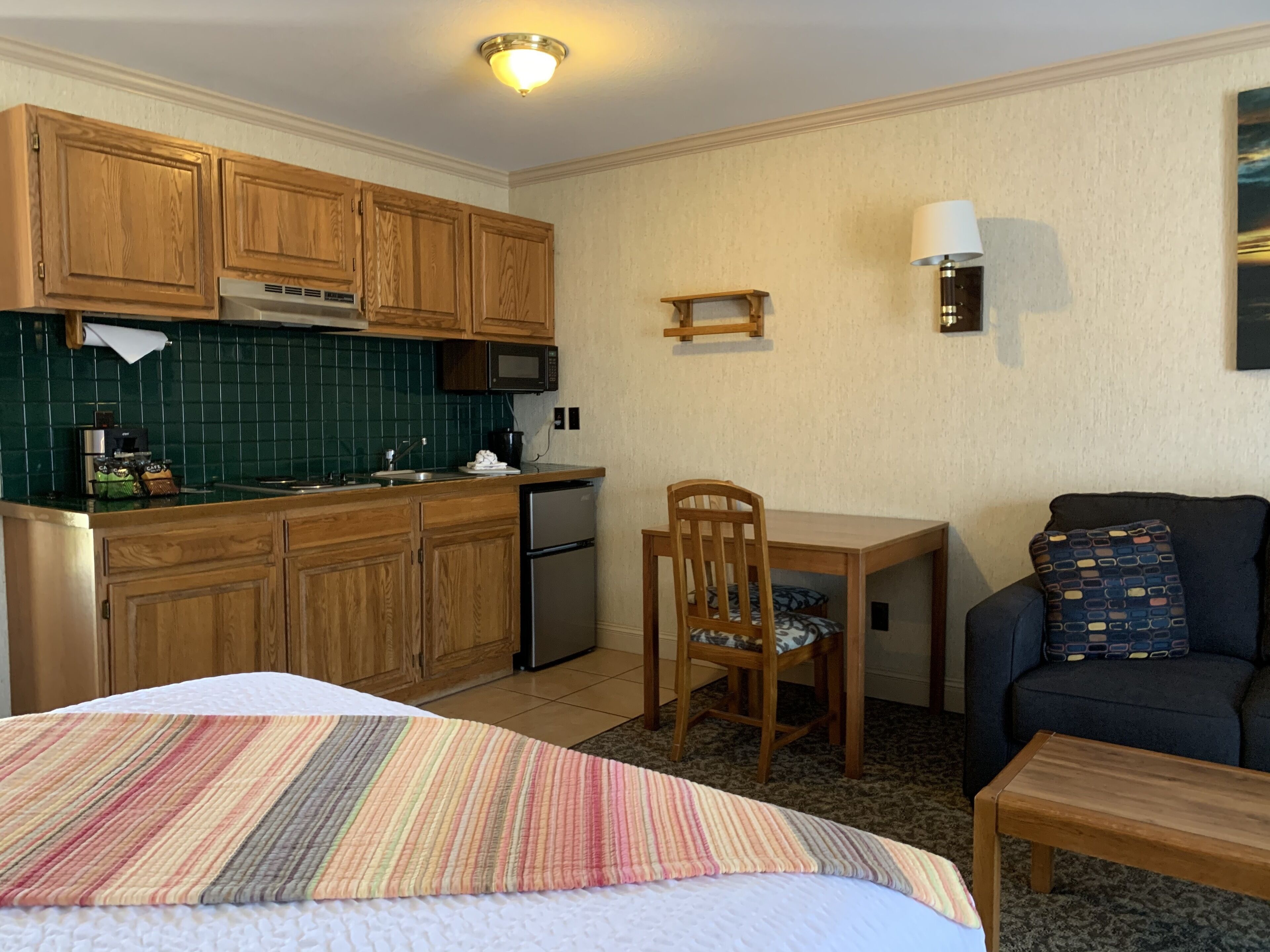 A compact kitchen with wooden cabinets, a microwave, and a sink. There's a dining area with a table, chairs, and a sofa.