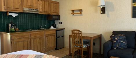 Una cocina compacta con armarios de madera, un microondas y un lavamanos. Hay una zona de comedor con una mesa, sillas y un sofá.