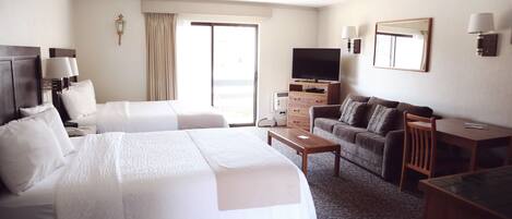 Ein Hotelzimmer mit zwei Betten, einer Couch, einem Fernseher und einem Schreibtisch.