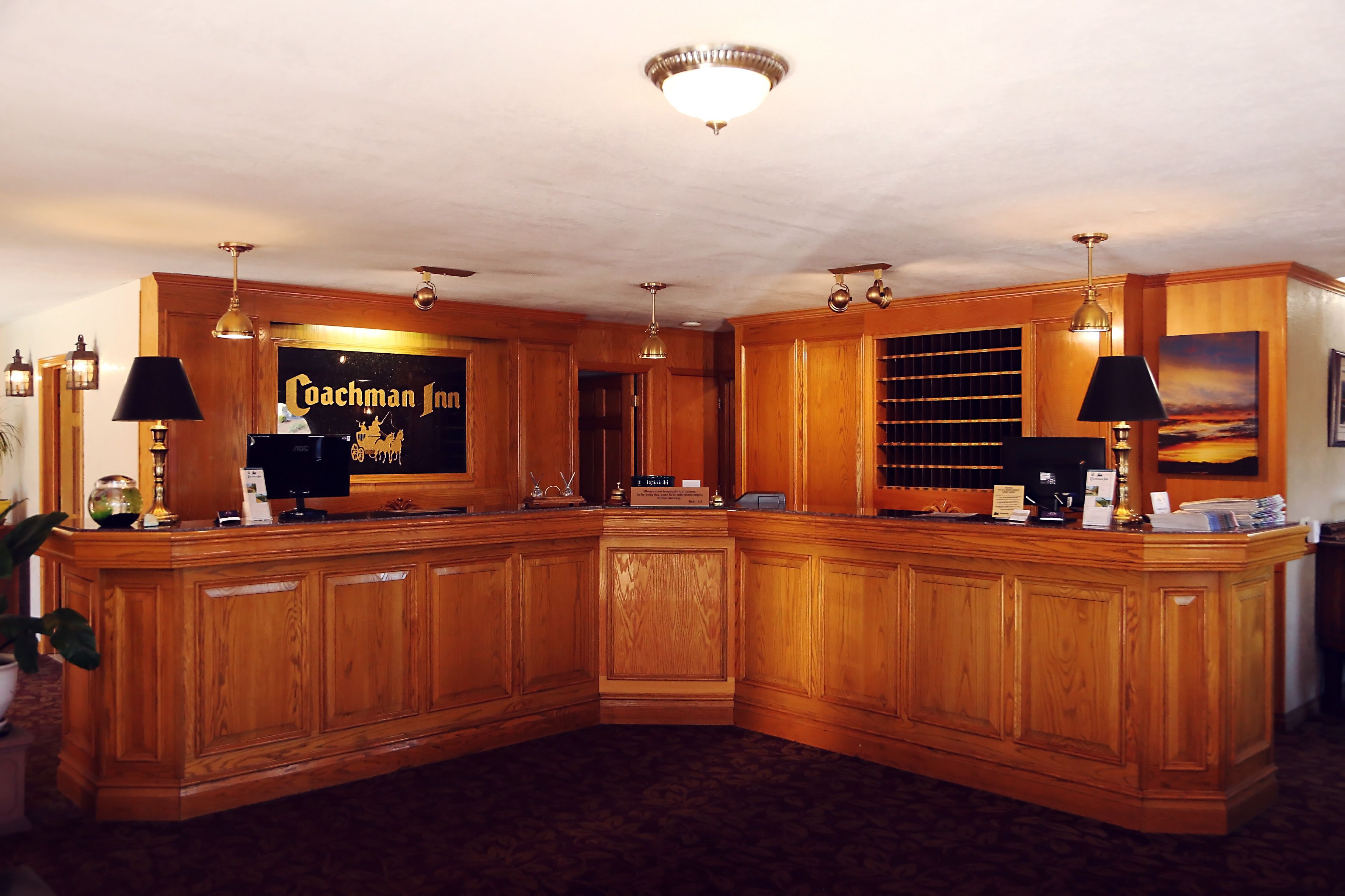 A reception area with a wooden reception desk, a television, and a framed sign that reads "Coachman Inn."