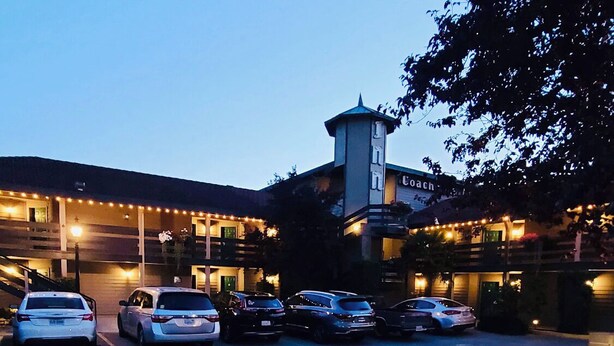 A hotel with a tower, multiple cars parked in the driveway, and string lights along the building's exterior.