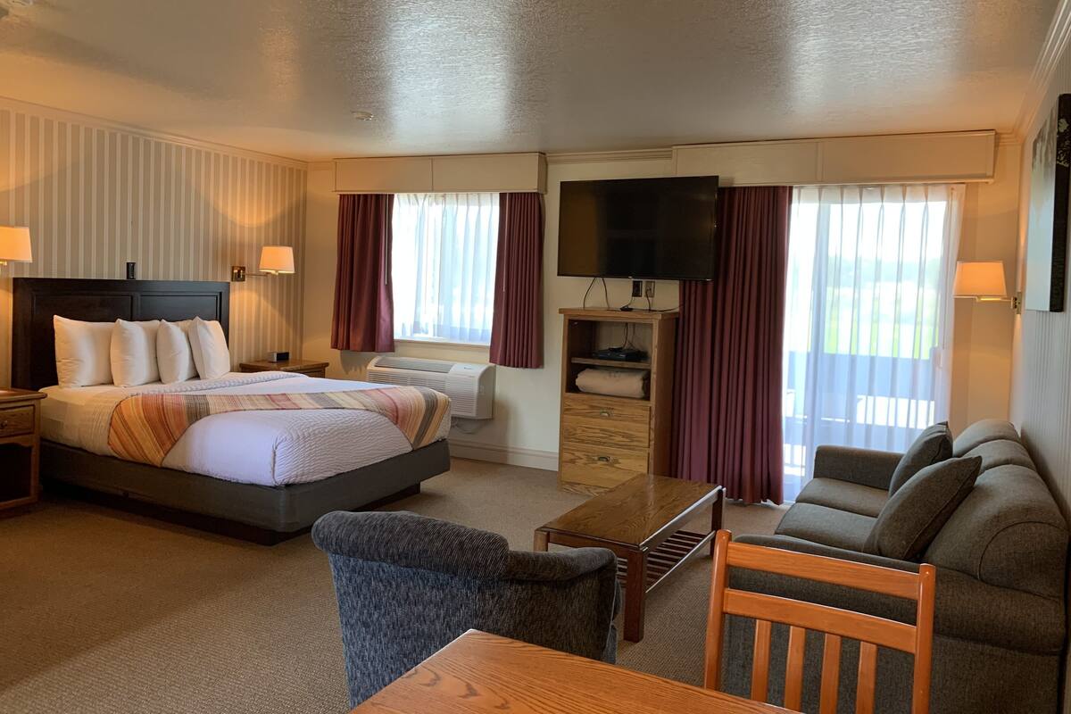 A hotel room with a large bed, a sofa, a TV, and a desk.