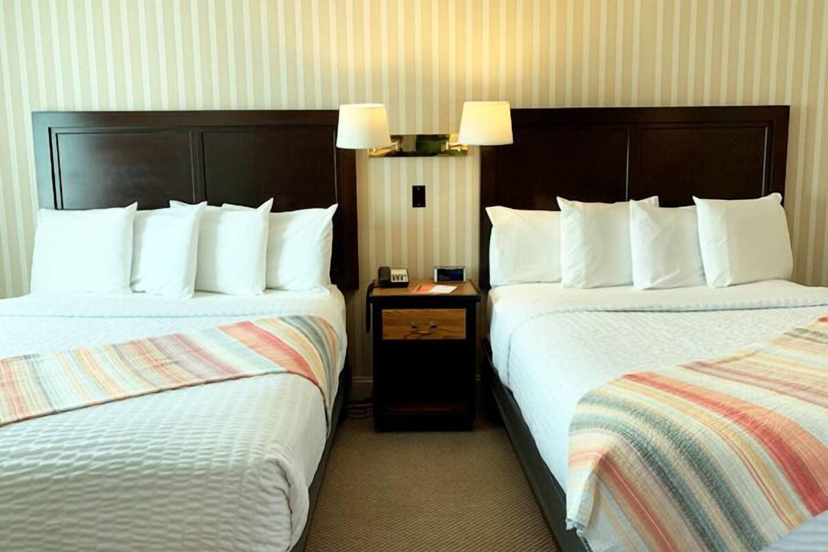 A hotel room with two beds, a nightstand with a lamp, and a striped blanket.