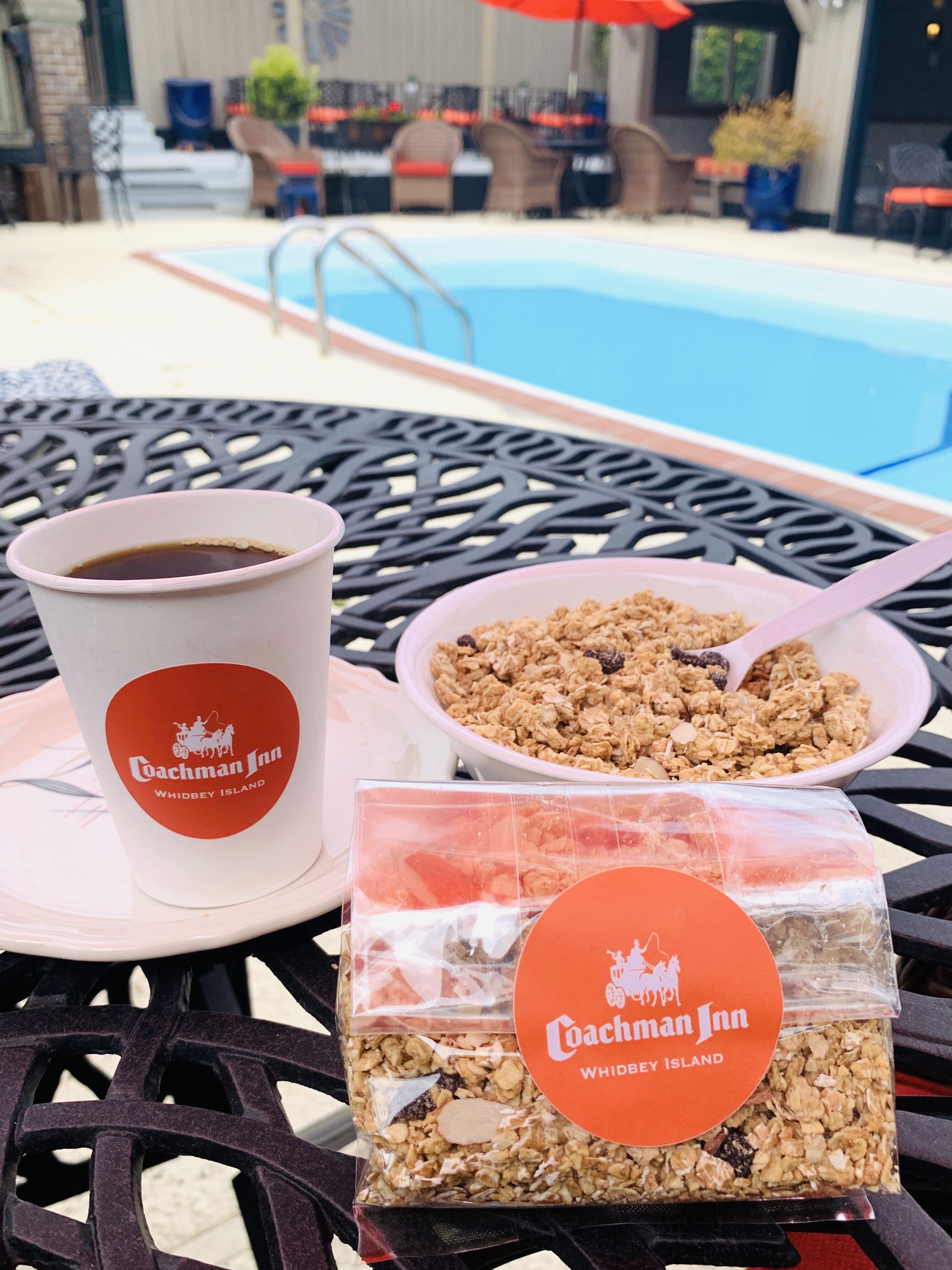 Un tavolo con una tazza di caffè, una ciotola di granola e una confezione di granola, in una zona vicino alla piscina.