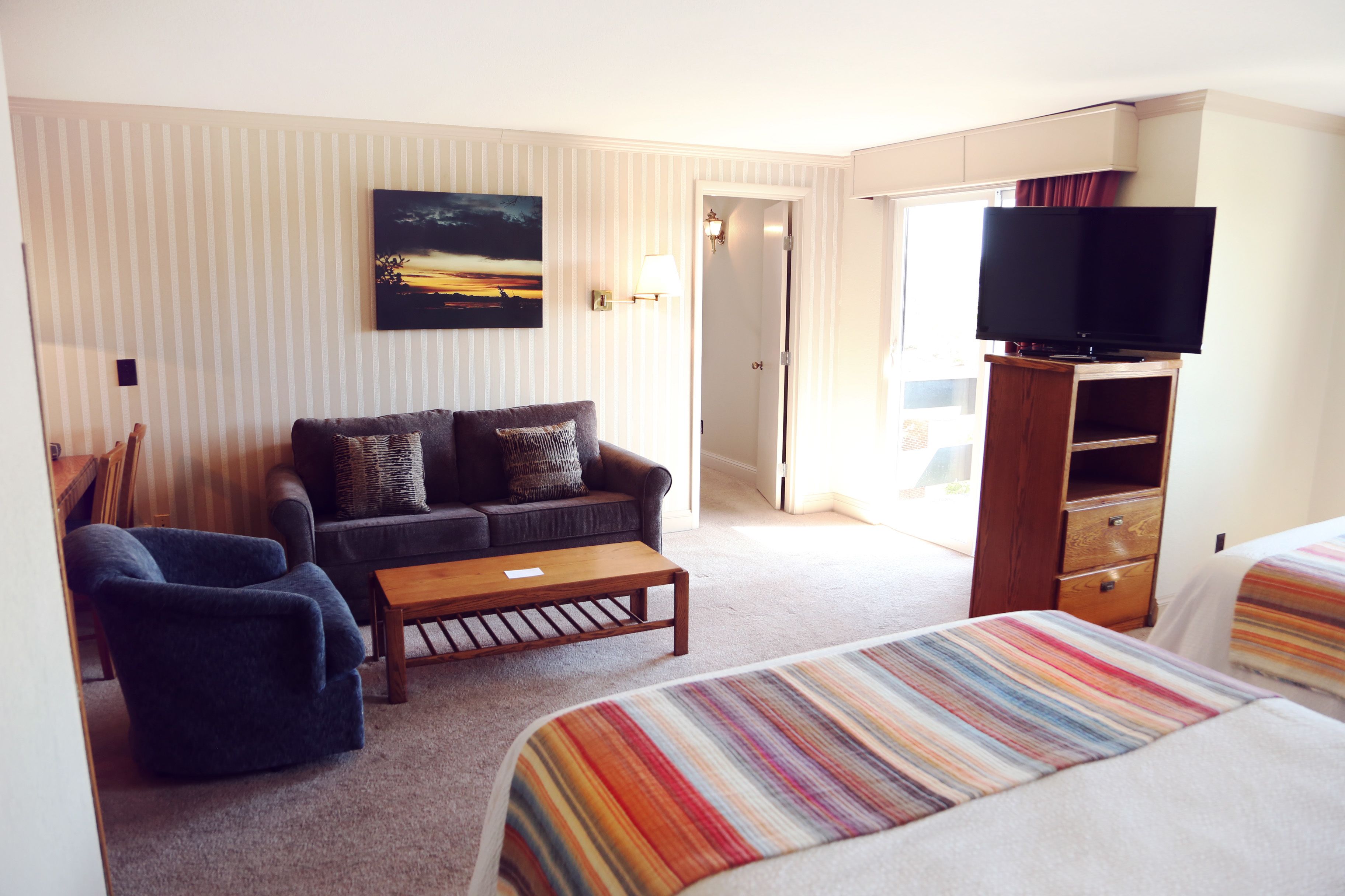 Una habitación de hotel con sofá, sillón y televisor sobre un mueble de madera.