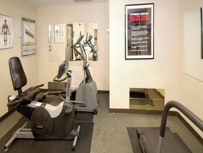 A fitness center with cardio equipment, a mirrored wall, and a poster with rules.
