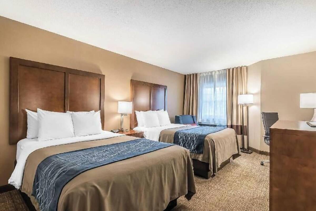 A hotel room with two beds, a desk, a chair, and a window with curtains.