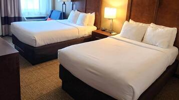 A hotel room with two beds, a desk, a chair, a lamp, and a window with curtains.