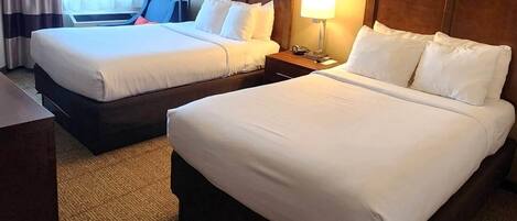 A hotel room with two beds, a desk, a chair, a lamp, and a window with curtains.