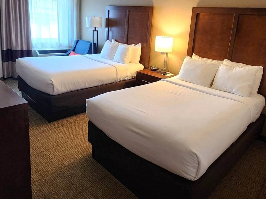 A hotel room with two beds, a desk, a chair, a lamp, and a window with curtains.
