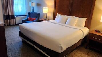 A hotel room with a large bed, a chair, a desk, and a lamp.